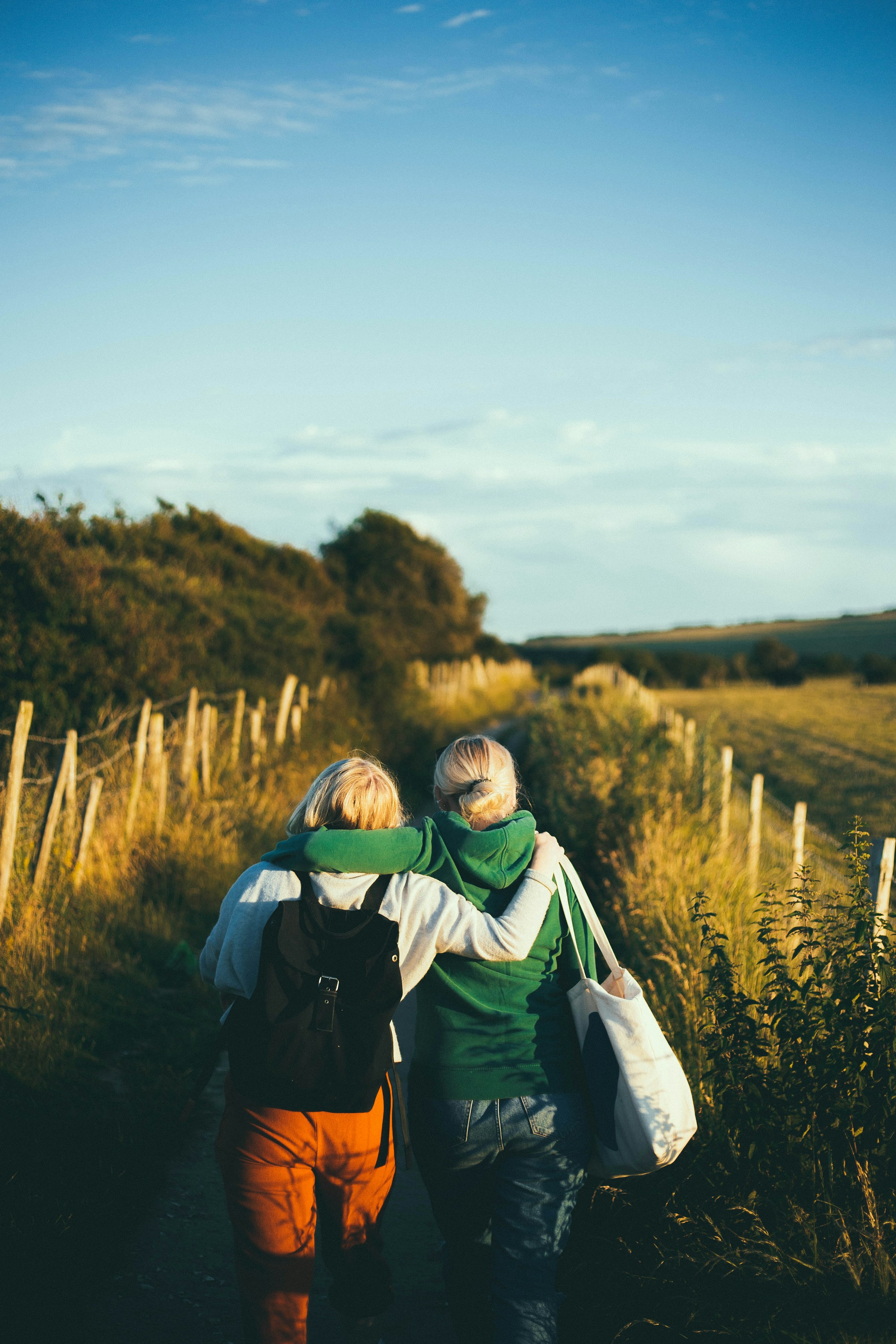 Two women walking arm in arm outdoors in the countryside, laughing together
